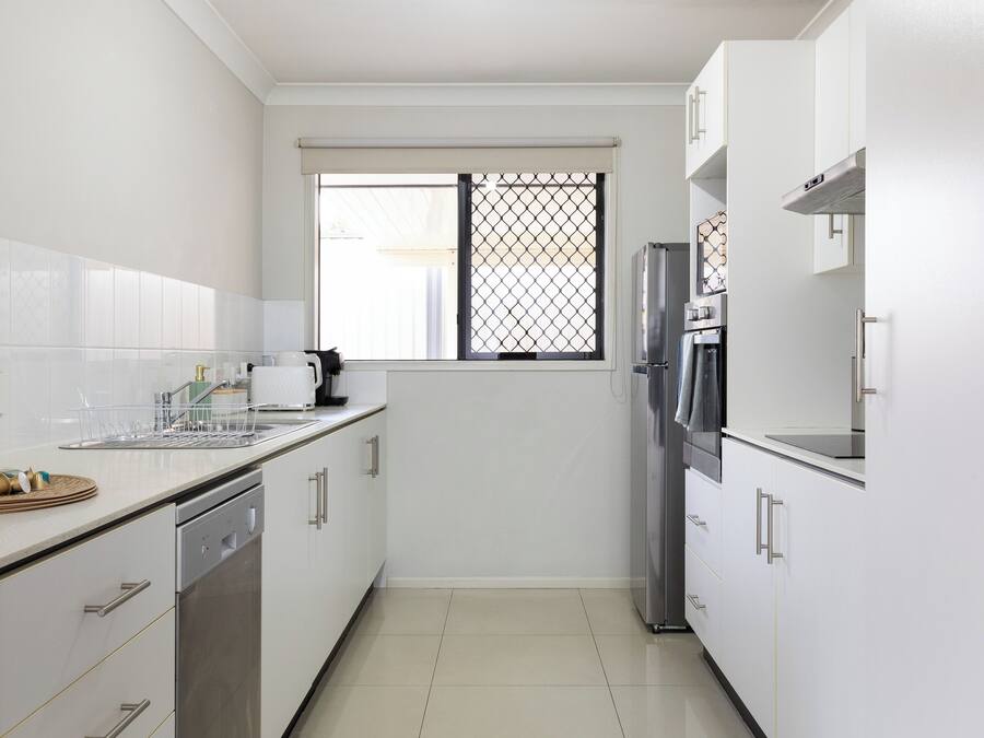 A compact kitchen with white cabinets, a dishwasher, a refrigerator, and a window with a metal screen.