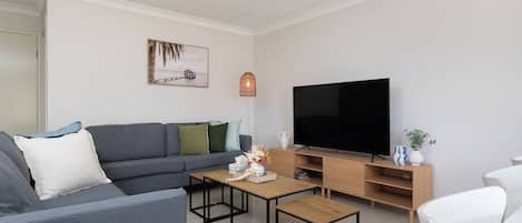 A modern living room with a grey sofa, a wooden coffee table, a TV, and a wooden TV stand.