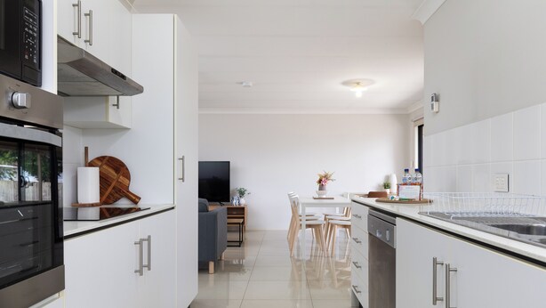 Una cucina moderna con mobili bianchi, elettrodomestici in acciaio inossidabile e una zona pranzo con sedie e tavolo in legno.
