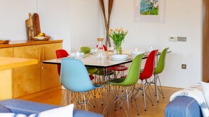Un comedor con una mesa de madera, sillas coloridas y un florero con flores.