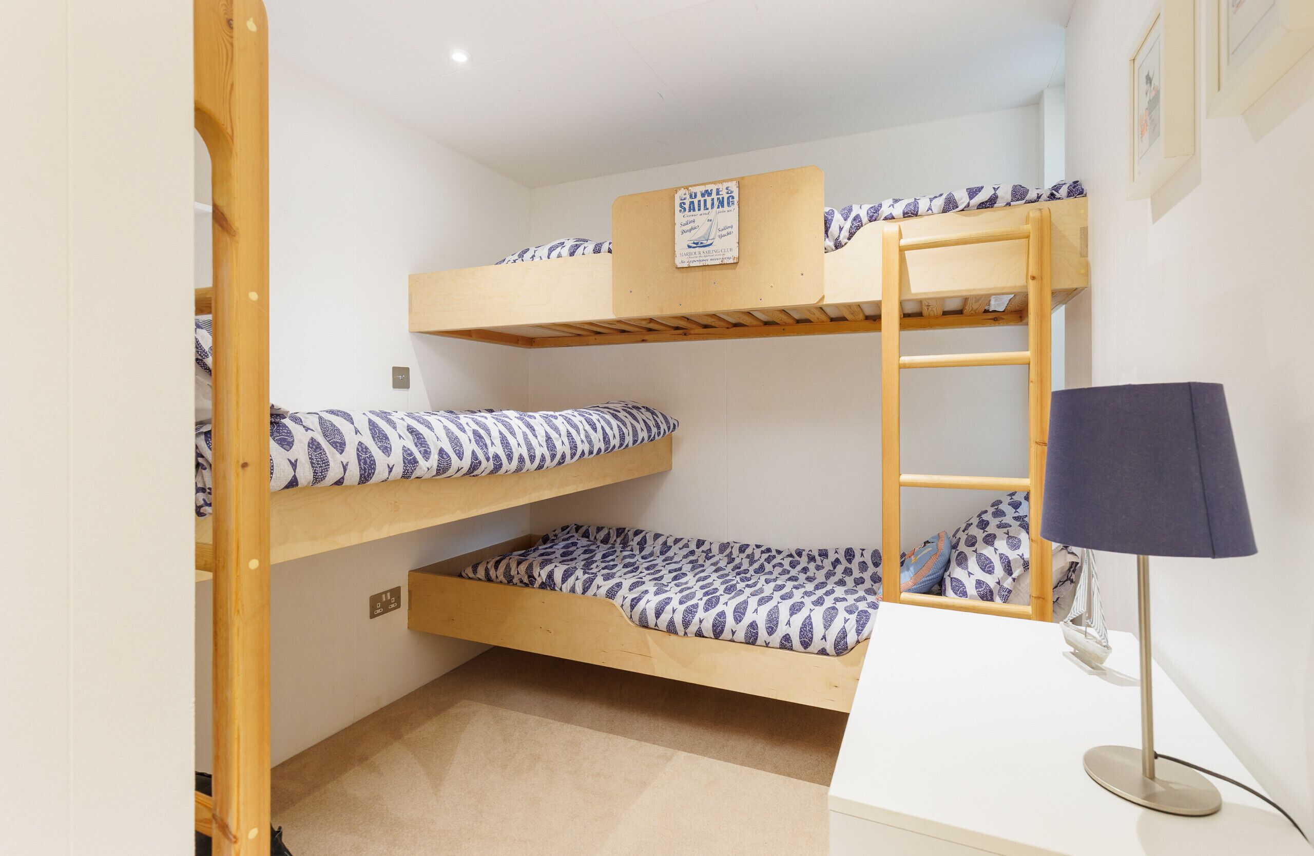 A bunk bed room with a desk and lamp, featuring a sign on the top bunk.