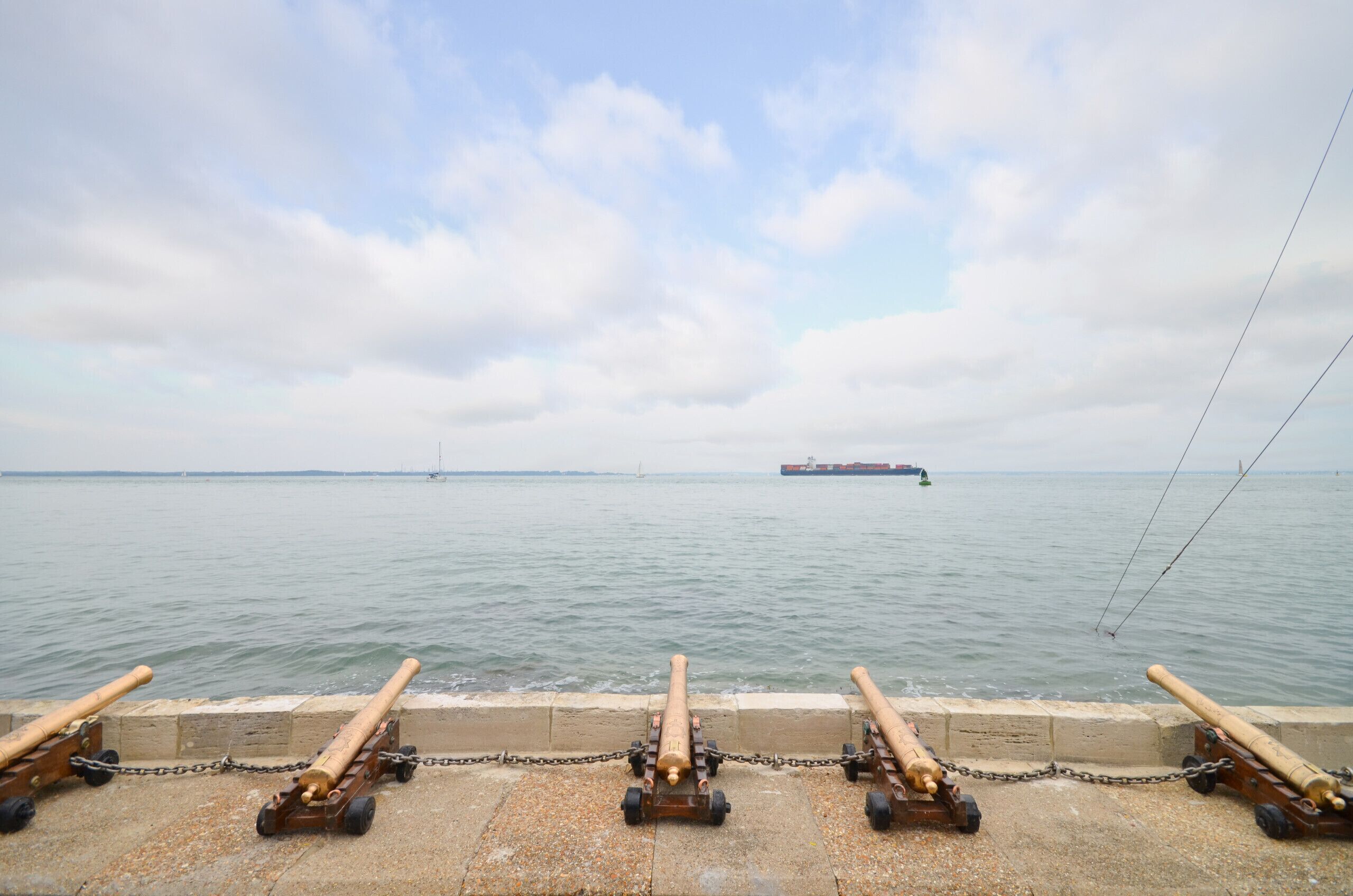A waterfront with cannons on display and a large ship in the distance.