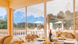 Uma área de refeições com uma mesa posta para dois, com vista para uma piscina e área de estar ao ar livre.