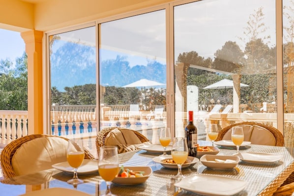 A dining area with a table set for two, overlooking a pool and outdoor seating.