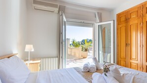 Quarto de hotel com cama, mesa de cabeceira com abajur, guarda-roupa de madeira grande e varanda com vista para o verde.