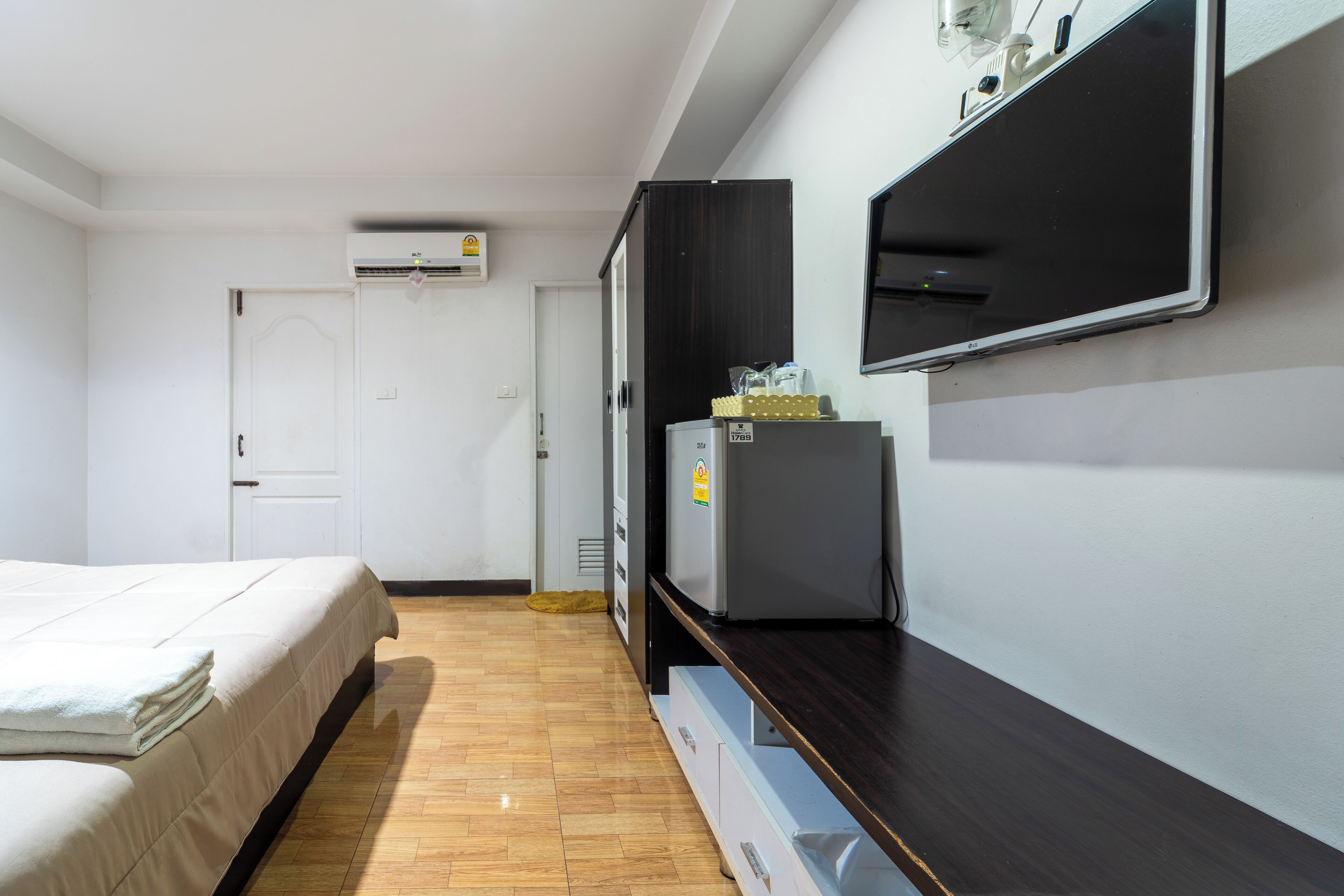 Une chambre d’hôtel équipée d’un lit, d’un téléviseur à écran plat fixé au mur, d’un réfrigérateur et d’un plancher en bois.