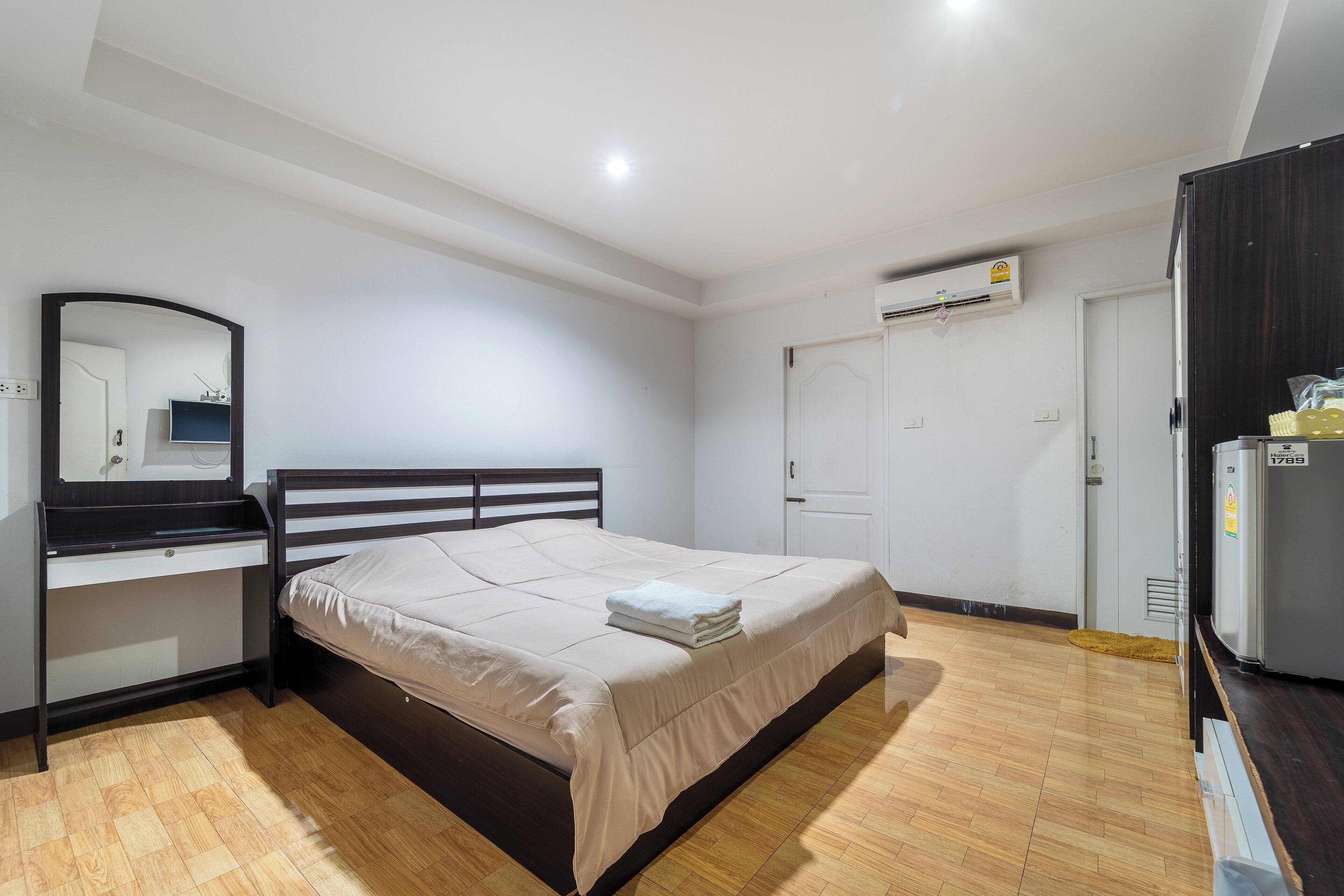 Un dormitorio con cama, escritorio, espejo, armario y equipo de aire acondicionado.
