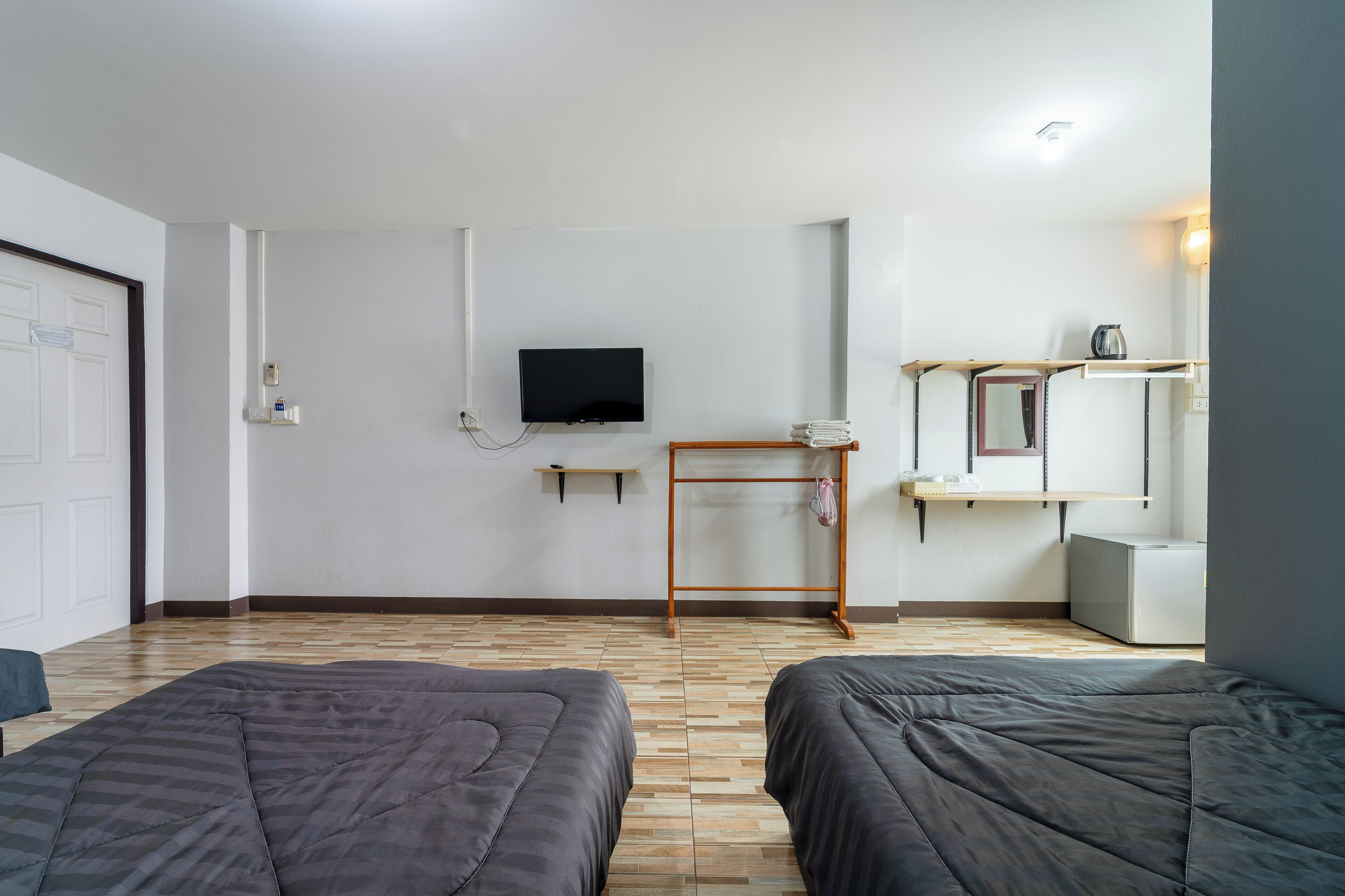 A room with two beds, a TV mounted on the wall, a small table, and a mirror.