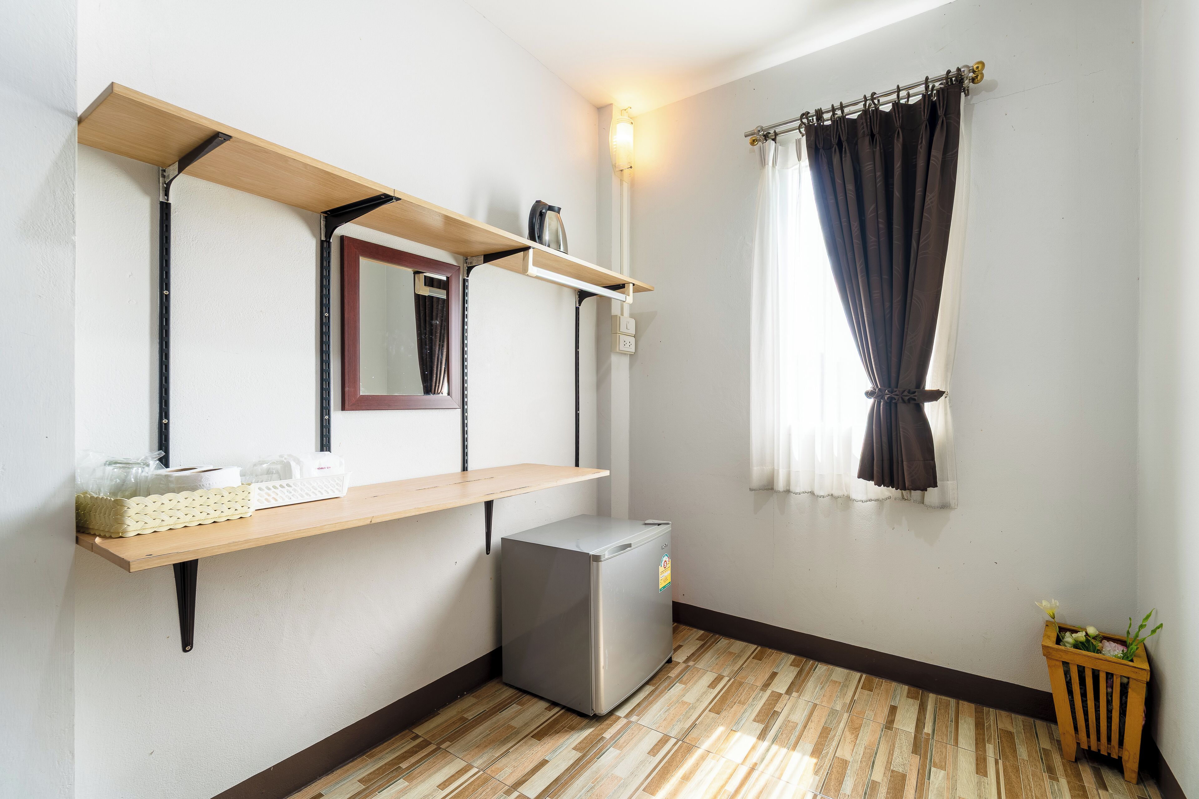 Una habitación compacta con un refrigerador pequeño, un estante de madera con un espejo y una ventana con cortinas.