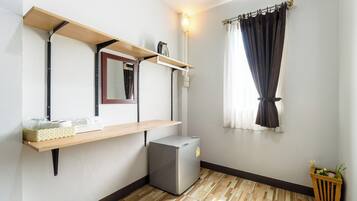 Una habitación compacta con un refrigerador pequeño, un estante de madera con un espejo y una ventana con cortinas.