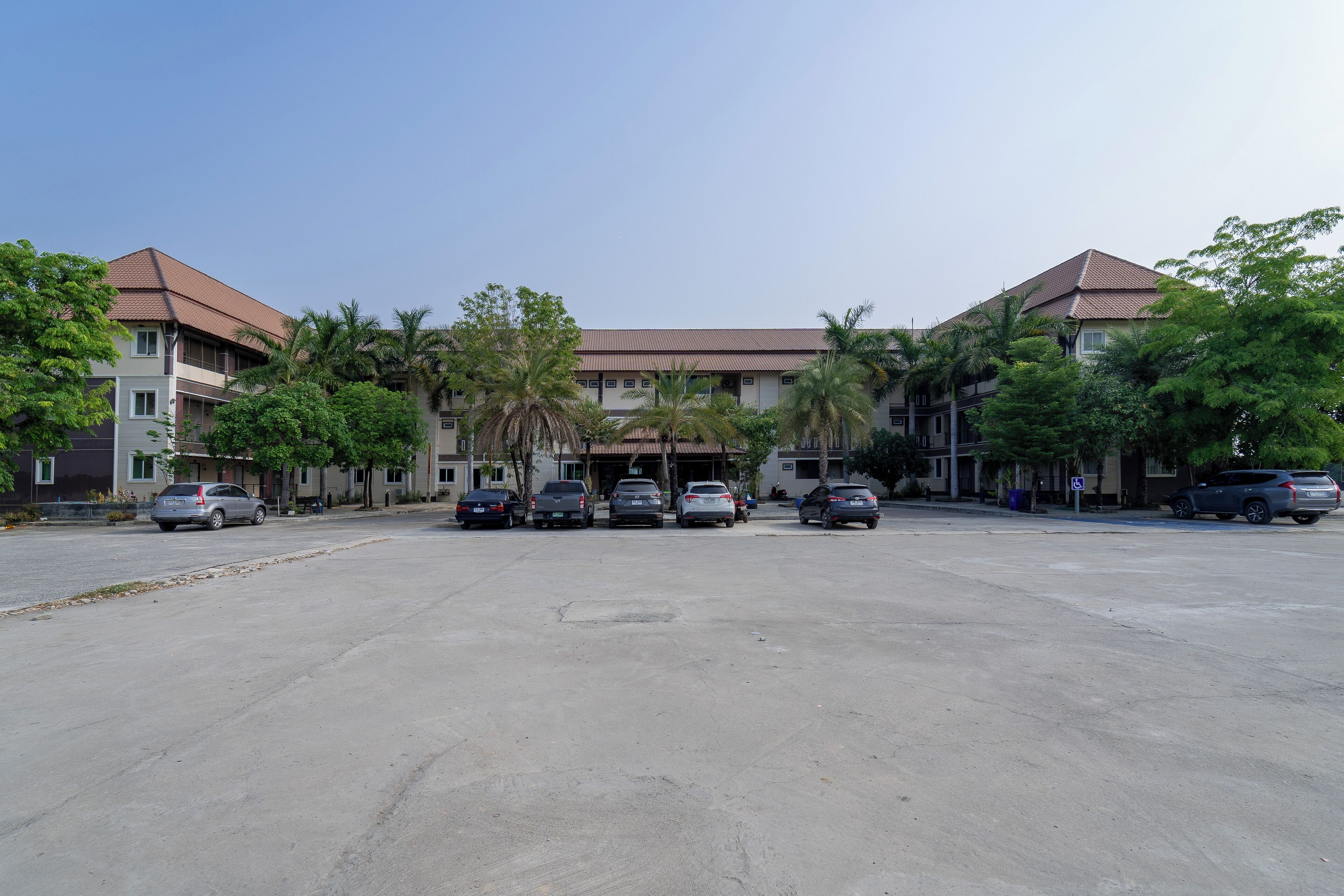 A parking lot with several cars, a building with a tiled roof, and palm trees.
