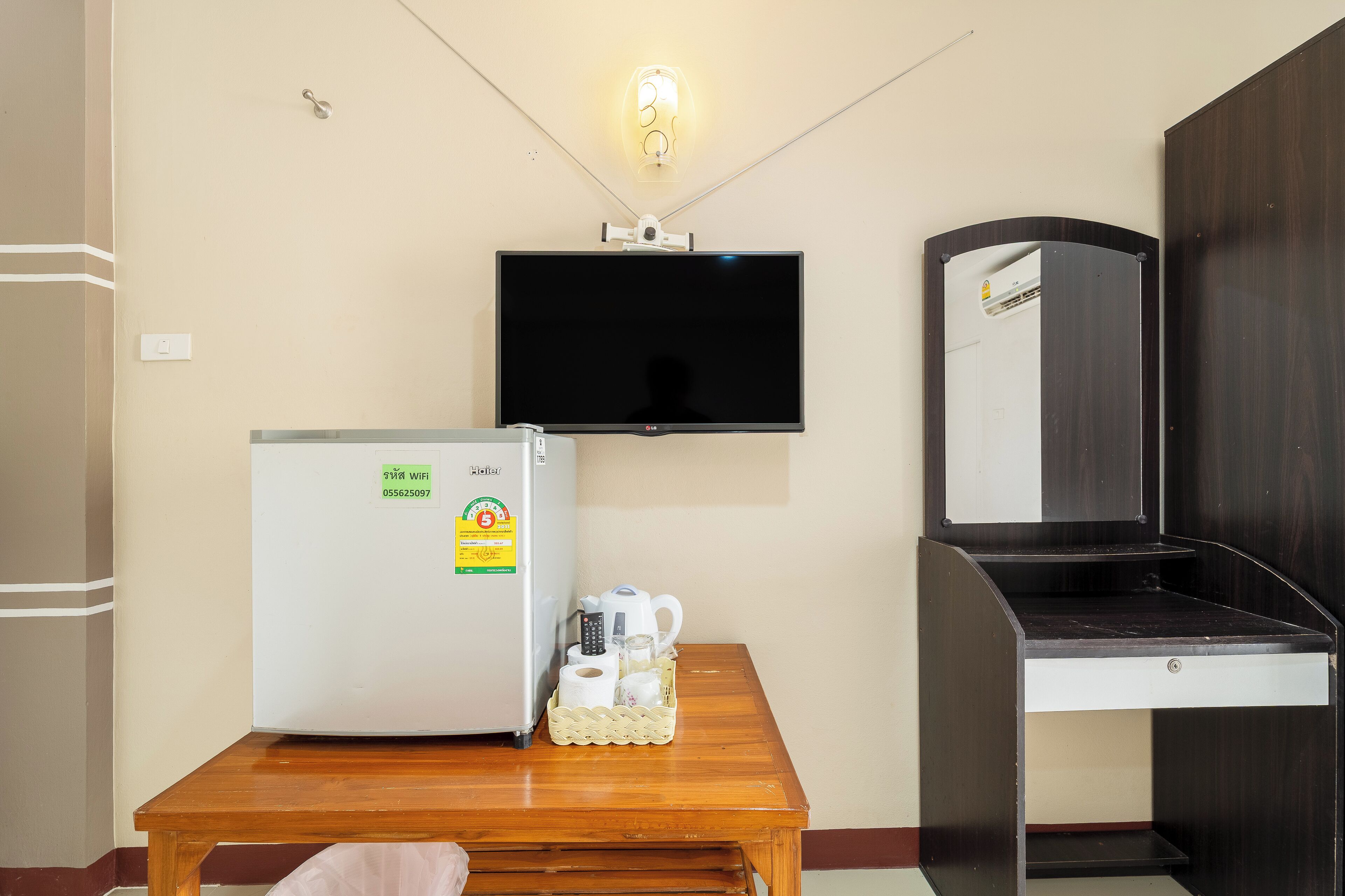 A room with a refrigerator, a flat-screen TV mounted on the wall, a wooden table, and a mirror cabinet.
