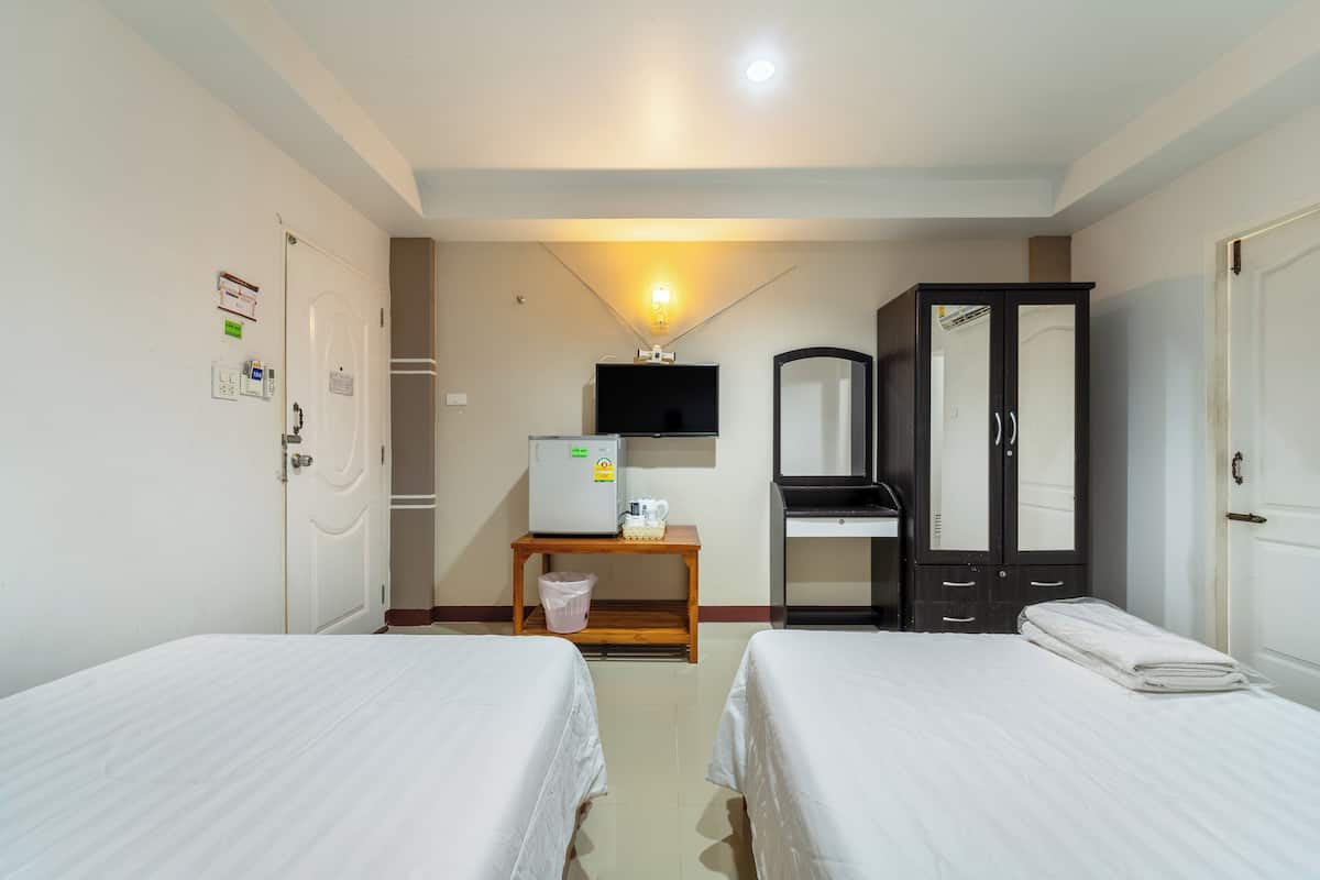 Une chambre d’hôtel avec deux lits simples, une petite table avec un réfrigérateur, une télévision et une armoire.