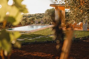 Área da piscina com espreguiçadeiras, um caminho de tijolos e vista para árvores e colinas ao fundo.