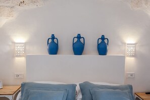 Quarto com uma cama, três vasos azuis numa prateleira branca e luminárias fixadas na parede.