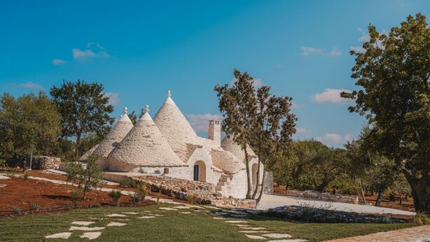 A white, pyramid-shaped building with a swimming pool in the foreground. - Luxury Apulian Villa inside Trulli with unique pool (Castellana Grotte)