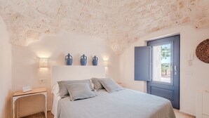 A bedroom with a bed, bedside tables, a wardrobe, and a door leading outside. - Luxury Apulian Villa inside Trulli with unique pool (Castellana Grotte)