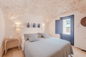 A bedroom with a bed, bedside tables, a wardrobe, and a door leading outside. - Luxury Apulian Villa inside Trulli with unique pool (Castellana Grotte)