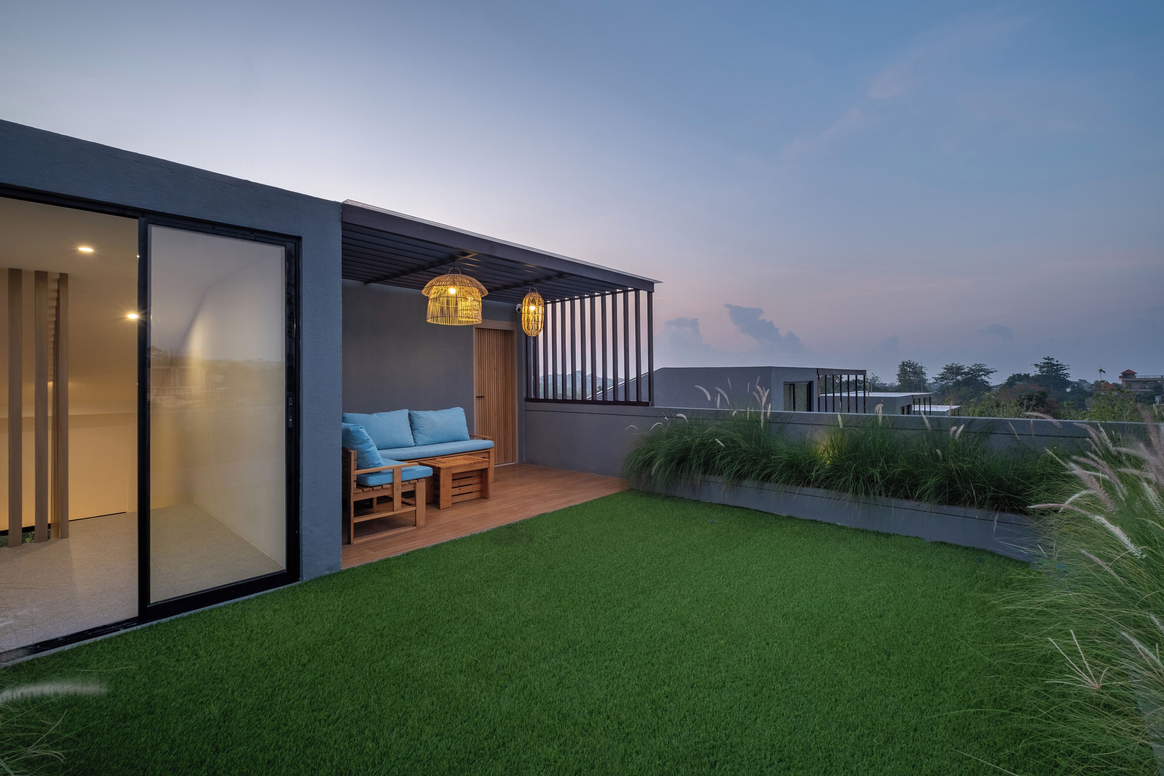A modern outdoor patio with a blue sofa, a wooden table, and two wicker lamps.