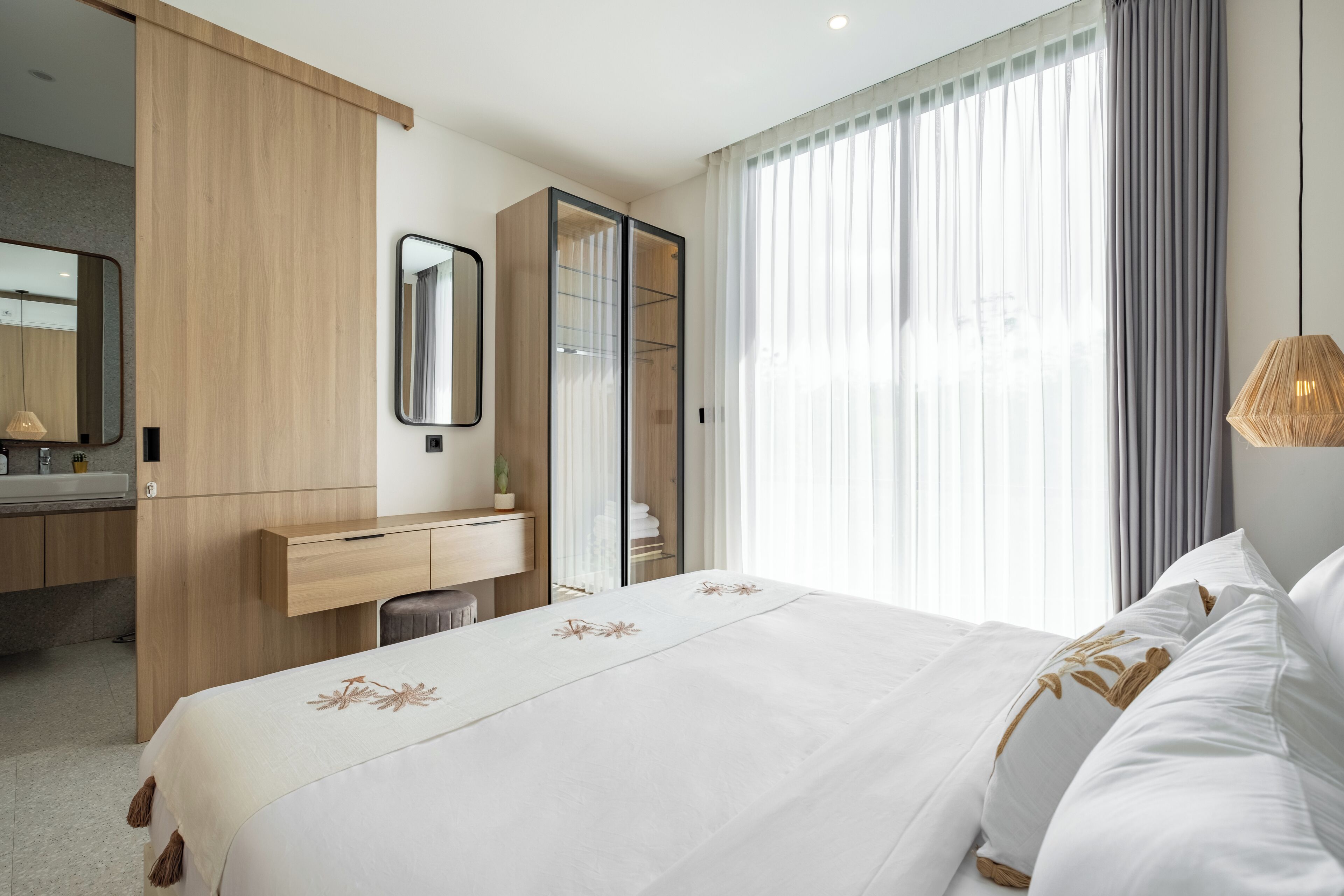 A hotel room with a bed, a wooden wardrobe, a desk, a mirror, and a window with curtains.