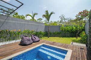 A backyard with a swimming pool, wooden deck, and various plants.