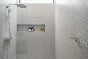 A modern shower area with a built-in shelf containing toiletries.