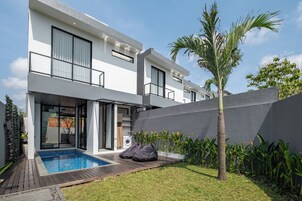 A modern two-story house with a swimming pool, a covered patio, and a small garden area with a palm tree.