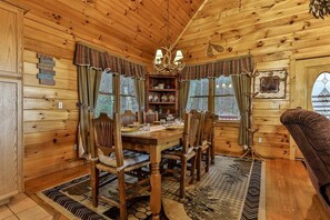 L’intérieur d’un chalet en bois, avec une table à manger, des chaises, un lustre et une cheminée.