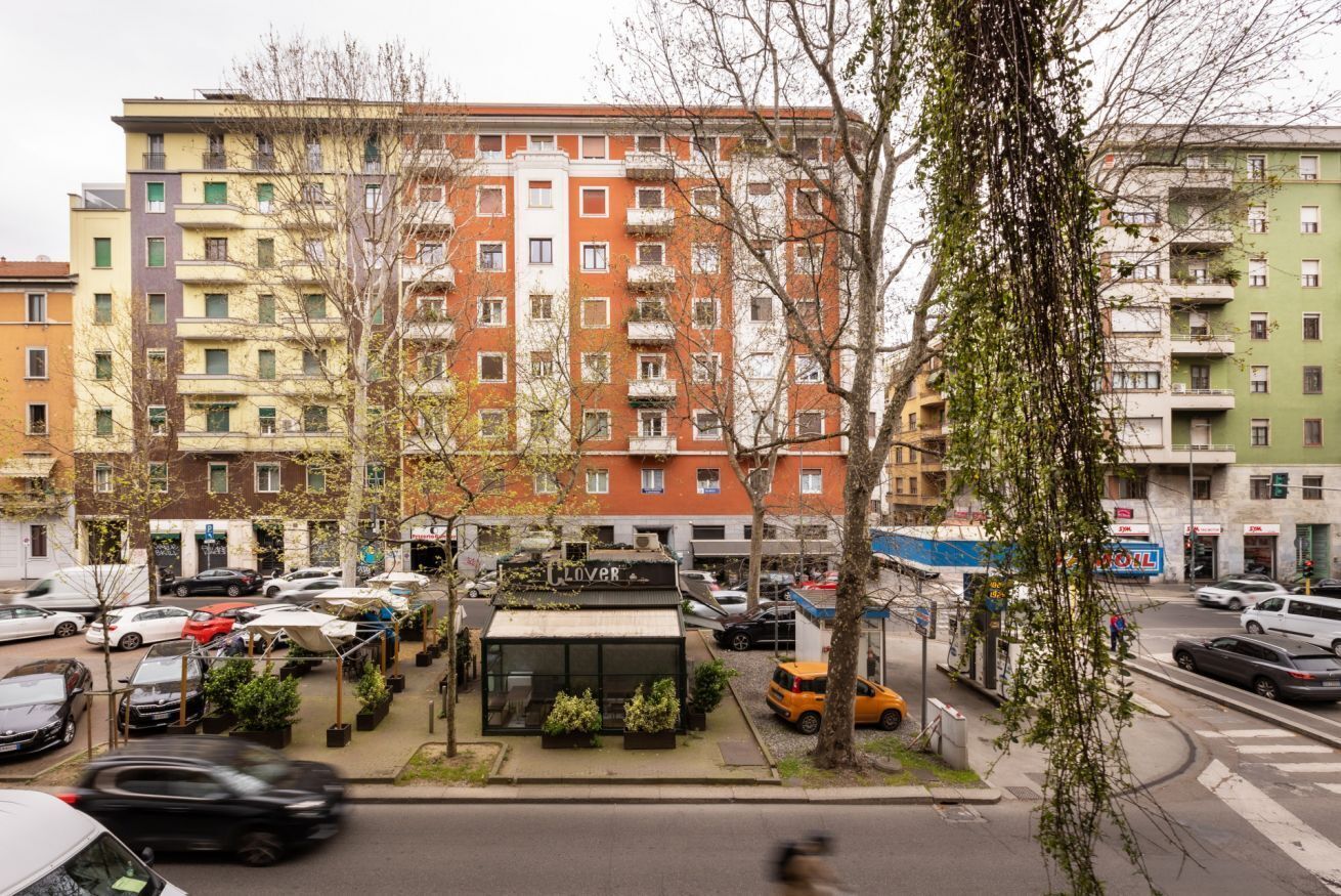 Un edificio residencial de varios pisos con balcones, un pequeño espacio al aire libre para sentarse y un escaparate visible.