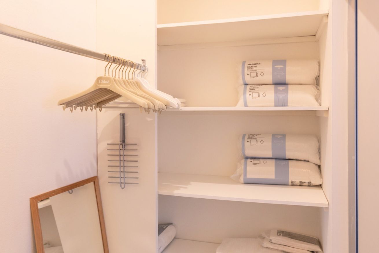 Un placard avec des vêtements suspendus, des étagères avec des serviettes pliées et un miroir.