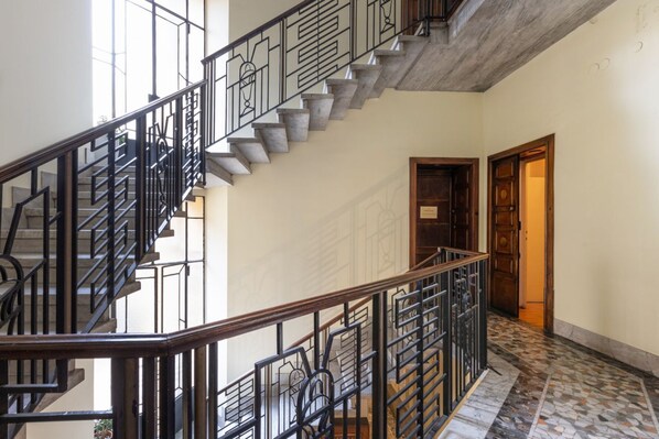 Una escalera con barandillas de metal negro y peldaños de piedra, que conduce a una puerta de madera.