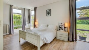 Un dormitorio moderno con cama, mesitas de noche y vistas al exterior.