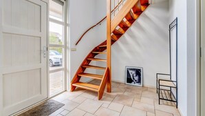 Un interior moderno con una escalera espiral de madera, una puerta blanca y un suelo de baldosas.