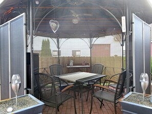 Une terrasse extérieure avec une table et des chaises, un espace abrité et une vue sur le jardin arrière.