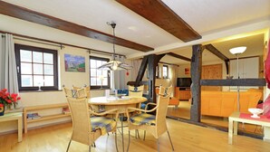 Een ruime kamer met een houten vloer, een eettafel met stoelen, een bank en een televisie.