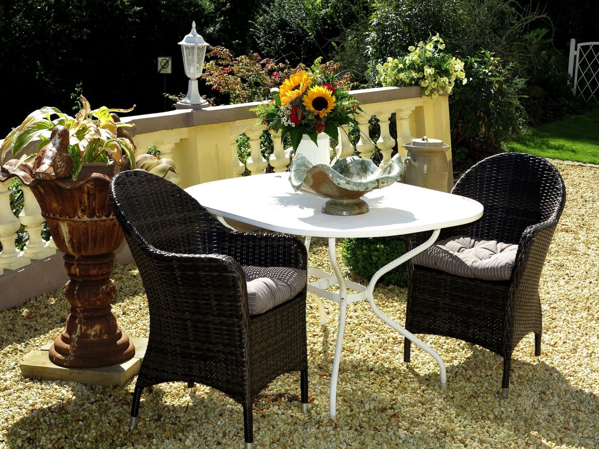 Een ronde tafel met twee rieten stoelen, een vaas met zonnebloemen en een decoratieve schaal.