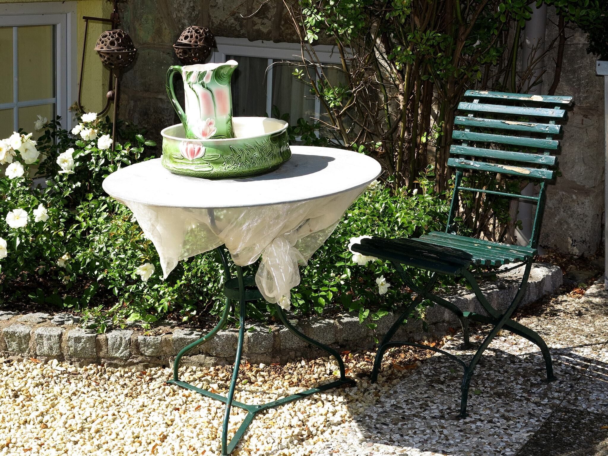 Uma mesa redonda com toalha branca e uma cadeira verde com estrutura metálica.