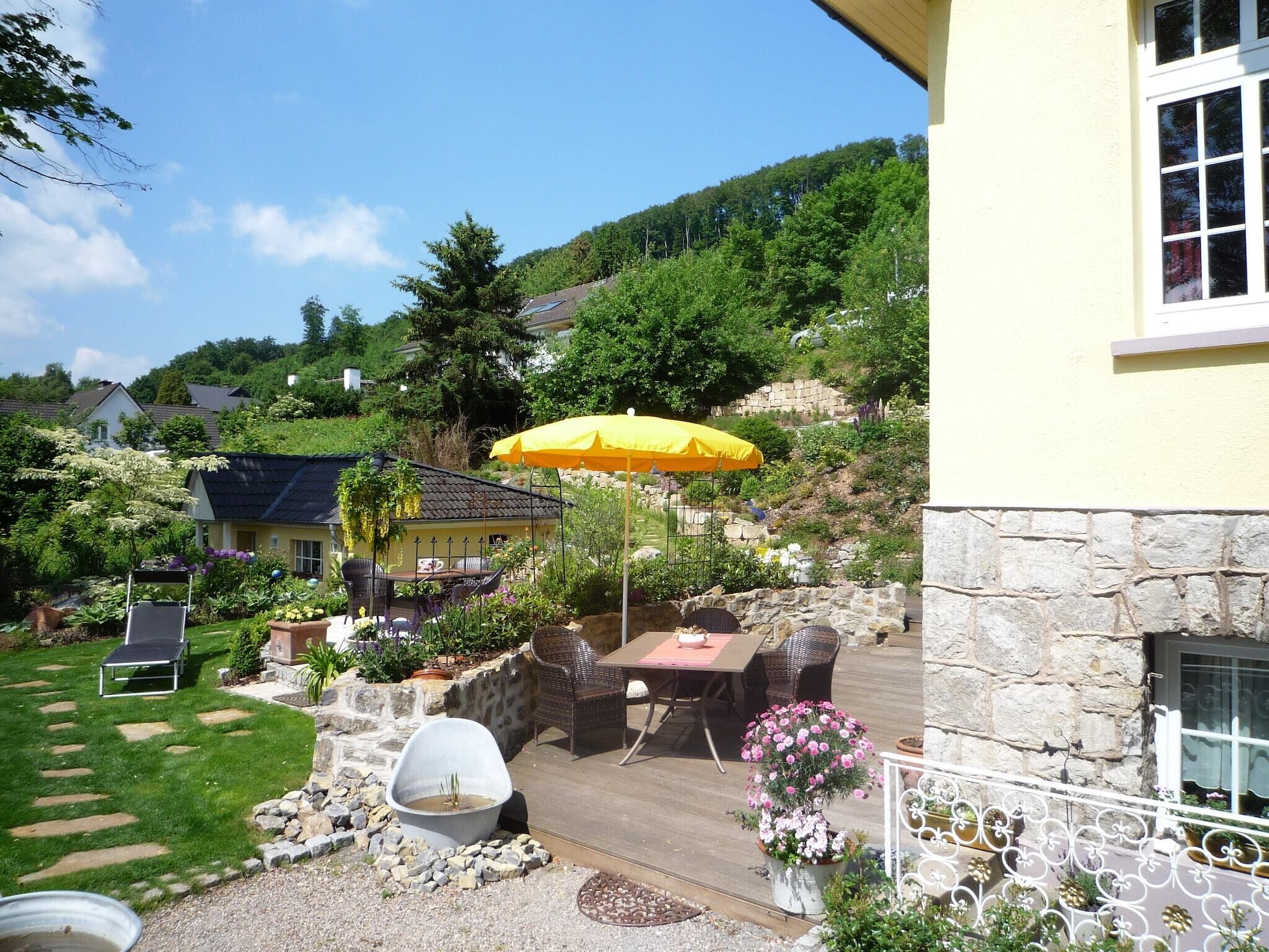 Eine Terrasse mit Gartenmöbeln, einem gelben Sonnenschirm und einer Steinmauer.