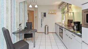 Een compacte keuken met een eethoek, uitgevoerd in een modern design met een roestvrijstalen spoelbak, een koffieapparaat en een kleine eettafel met stoelen.