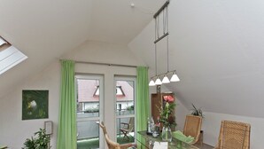 Een eetruimte met een glazen tafel, rieten stoelen, een groen gordijn en uitzicht op het omliggende landschap.