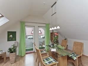 Een eetruimte met een glazen tafel, rieten stoelen, een groen gordijn en uitzicht op het omliggende landschap.