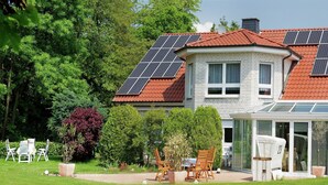 Een huis met een rood pannendak, zonnepanelen en een tuinkamer.