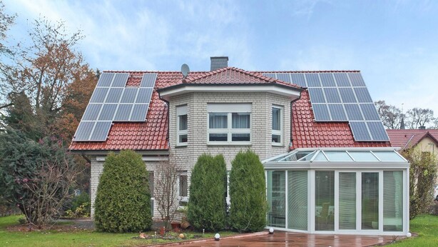 Een huis met zonnepanelen op het dak, een conservatorium en een verzorgde tuin.