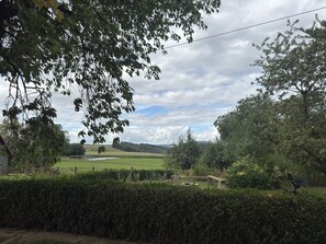 A rural landscape with a hedge in the foreground, a wooden bench, and a distant view of a field and wind turbines. - Ferienwohnung mit Garten auf dem Bauernhof (Trendelburg-Friedrichsfeld)