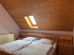 A bedroom with a sloped ceiling, a skylight, a bed with striped bedding, a bedside table, and a nightstand. - Ferienwohnung mit Garten auf dem Bauernhof (Trendelburg-Friedrichsfeld)