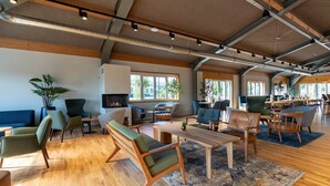 Un'ampia e luminosa area relax con pavimenti in legno, diverse opzioni di seduta tra cui divani e poltrone, e ampie finestre che lasciano entrare luce naturale.