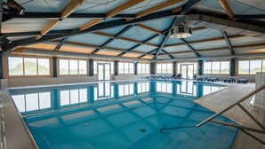 Una piscina interna con soffitto alto, ampie finestre e pavimento piastrellato.