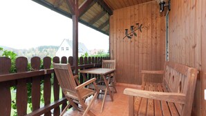 Een houten terras met twee houten stoelen en een tafel, met uitzicht op een groen landschap met huizen.