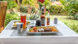 Une table dressée avec un repas, des boissons, des condiments et une rose.