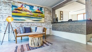 A reception area with a wooden reception desk, a sofa with striped cushions, a round wooden coffee table, and a painting of tropical birds on the wall. - St. Anastasia Hotel (Burgas)